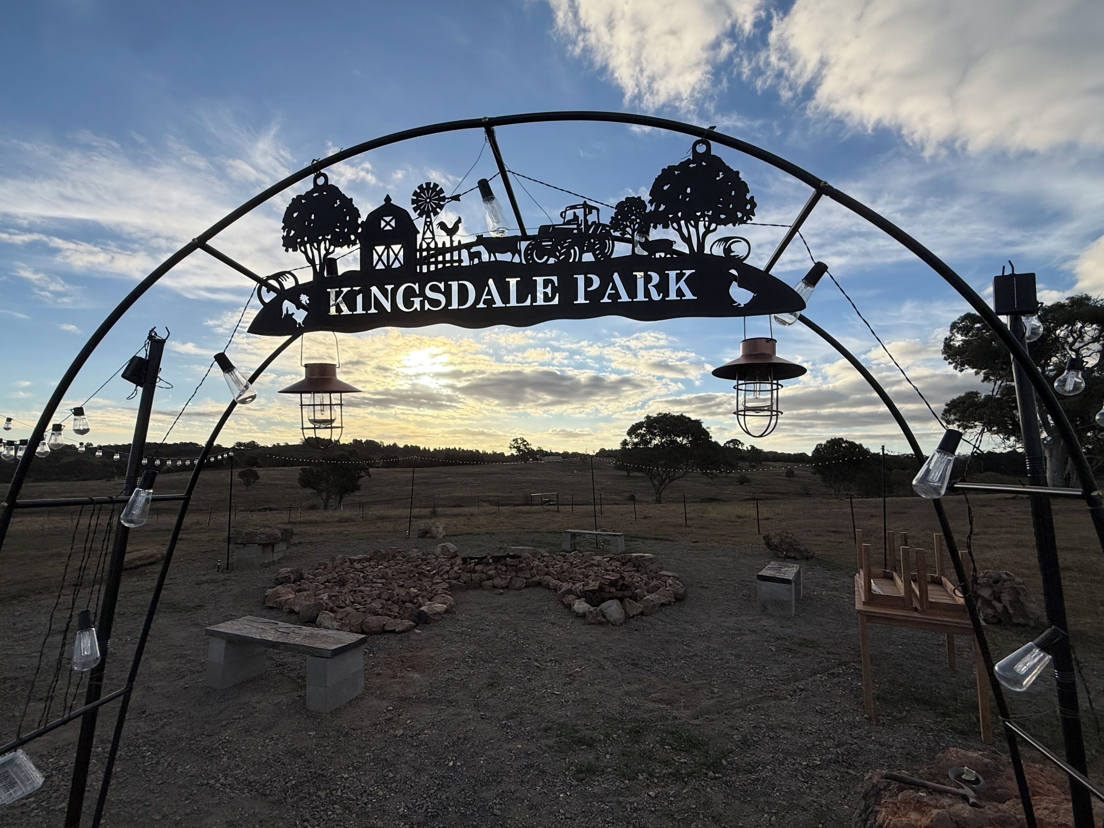 A sign for Kingsdale Park with a rustic design, including silhouettes of trees, a windmill, and farm animals.