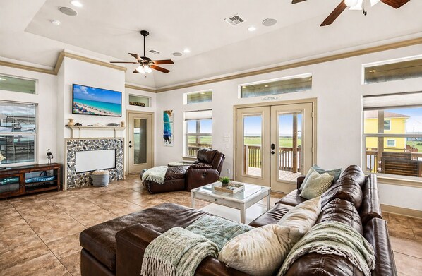 A spacious living room with a fireplace, a large TV, and a ceiling fan. - Crystal Beach | 4BR | Sleeps 22 | Decks (Port Bolivar)