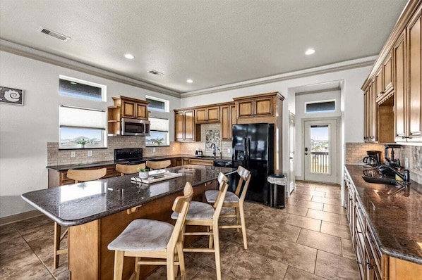 A spacious kitchen with a large island, wooden cabinets, and a black refrigerator. - Crystal Beach | 4BR | Sleeps 22 | Decks (Port Bolivar)