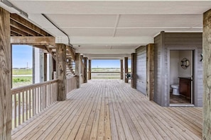 A covered wooden deck with a view of the landscape, a staircase, and a bathroom visible through an open door. - Crystal Beach | 4BR | Sleeps 22 | Decks (Port Bolivar)
