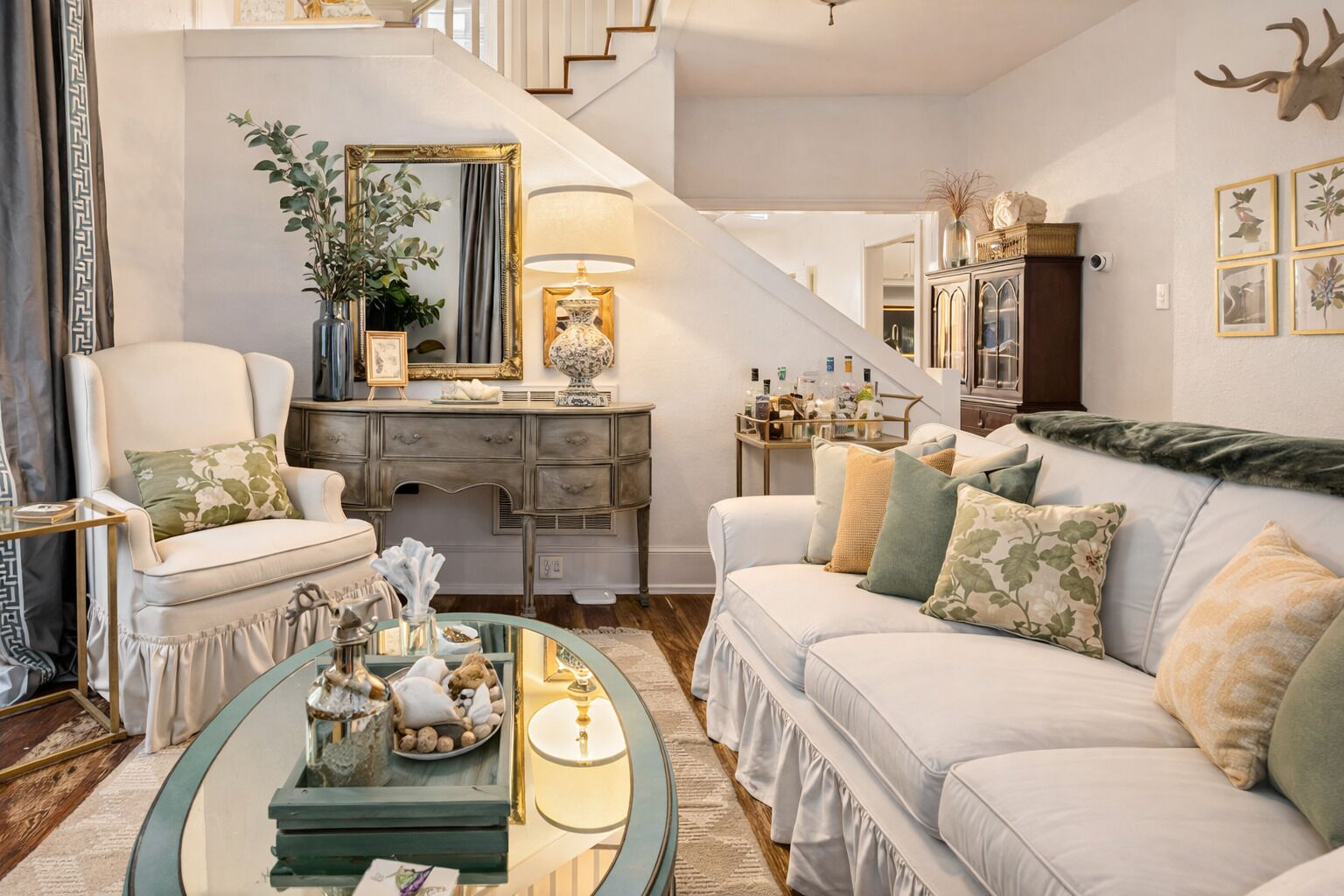 Una sala de estar con sofá, sillón, mesa de centro y una escalera que sube a otro nivel.