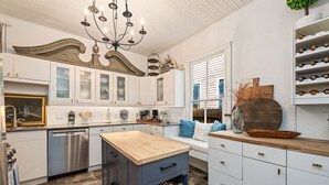 Una cocina con armarios blancos, encimera de madera, candelabro y una estantería empotrada para vinos.