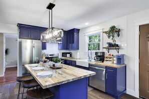 Eine moderne Küche mit blauen Schränken, einer Holztresle, Edelstahlgeräten und einer hängenden Pflanze.