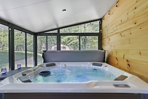 Ein Whirlpool mit Blick auf einen Wald, große Fenster und ein Holzinnenraum.