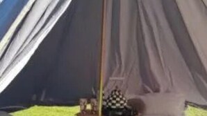 Ein Zelt mit Schlafbereich, einem kleinen Tisch mit kariertem Tuch und einer Lampe.