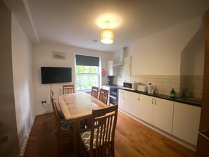A modern kitchen with white cabinets, a wooden dining table, and a flat-screen TV mounted on the wall. - Apartment Sleeps 10 with City Views (London)