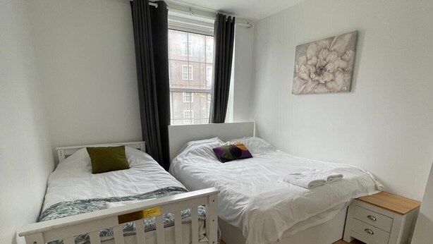 Une chambre avec deux lits simples, une fenêtre avec des rideaux, une table de chevet et un luminaire suspendu.