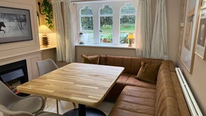 Une pièce chaleureuse avec une table en bois, un canapé en cuir marron, un tableau encadré et une fenêtre avec des rideaux.