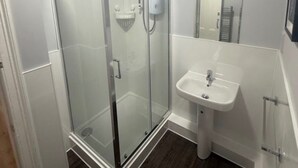 Et moderne badeværelse med en glasbrusekabine, en hvid vask og et spejl.