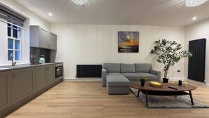 Et moderne køkken med lysegrå skabe, et spiseområde med en grå sofa, et sofabord og et billede på væggen.