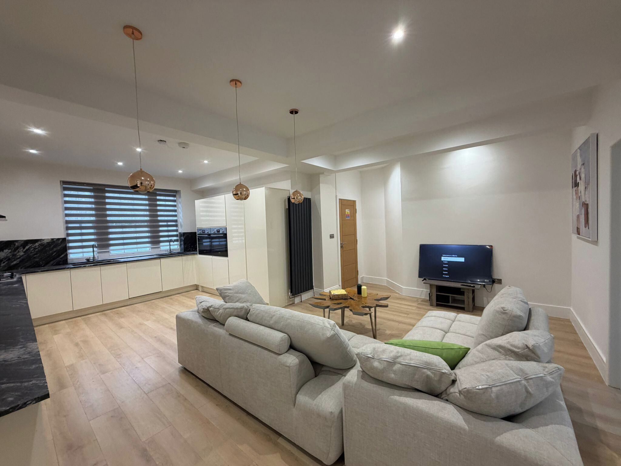 A modern living room with a sofa, TV, and kitchen in the background.
