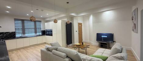 A modern living room with a sofa, TV, and kitchen in the background.