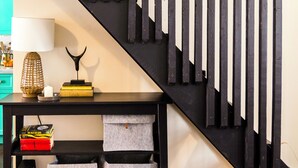 A staircase with black railings and a wooden handrail, a black console table with storage boxes, and a teal-colored wall. - The blacksmith's shop - L'atelier de forgeron (Québec)