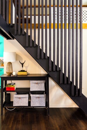 A staircase with black railings and a wooden handrail, a black console table with storage boxes, and a teal-colored wall. - The blacksmith's shop - L'atelier de forgeron (Québec)