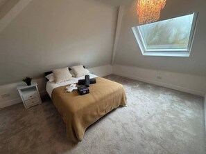 Een slaapkamer met een bed, nachtkastje, lamp en een raam.