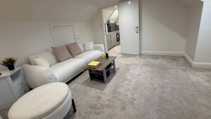 En moderne stue med en hvid sofa, en rund skammel, et sofabord og et lille plantebord.