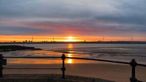 Un atardecer sobre un cuerpo de agua con el horizonte de una ciudad distante y aerogeneradores.