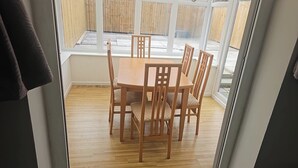 Un comedor con mesa y sillas de madera, ventanas amplias y vista a una cerca de madera al exterior.