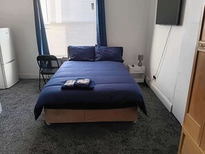 Habitación de hotel con cama, una silla, escritorio, lámpara y televisión.