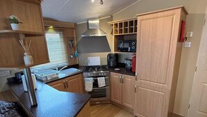 A compact kitchen with a stove, microwave, and sink. - 2-Bed Caravan, Sleeps 6 w/ Parking, No Pass Needed (Abergele)