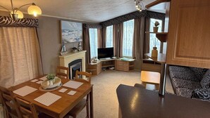 A cozy living room with a fireplace, television, and dining area. - 2-Bed Caravan, Sleeps 6 w/ Parking, No Pass Needed (Abergele)