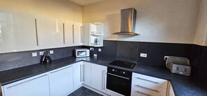 A modern kitchen with white cabinets, a black countertop, a stove, a microwave, and a toaster.