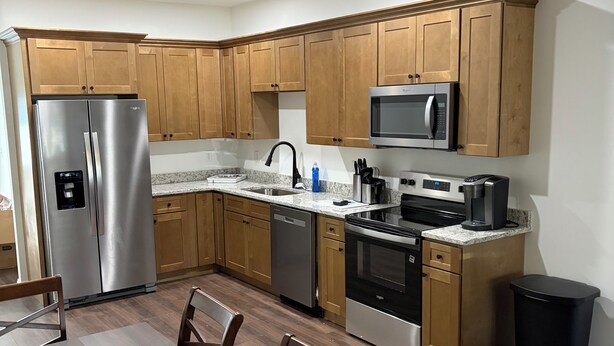 Una cocina moderna con armarios de madera, electrodomésticos de acero inoxidable, una encimera de granito y un comedor con mesa y sillas.