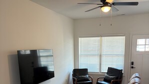 Una sala de estar con sofá, sillones, televisor, ventilador de techo y una puerta.