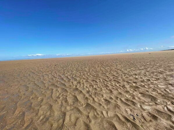 Ein sandiger Strand mit Fußspuren und einem strahlend blauen Himmel.