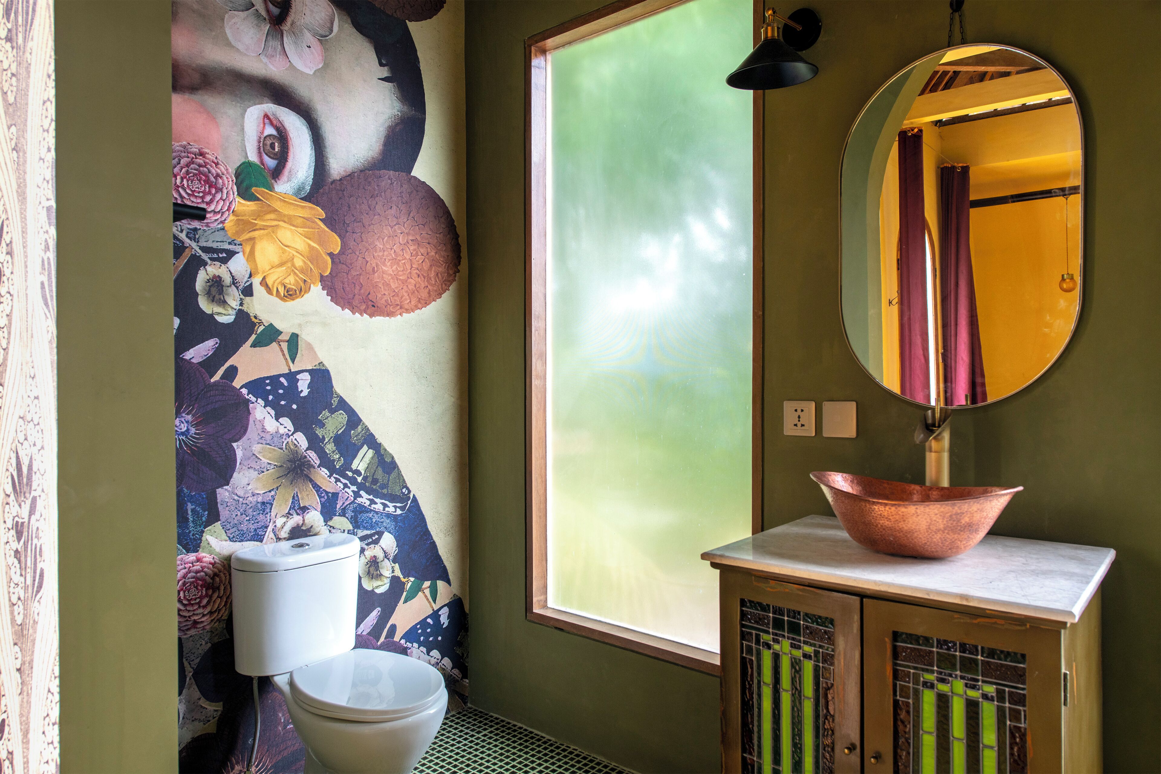 A bathroom with a toilet, a sink with a copper basin, a mirror, and a window with a view of a building.