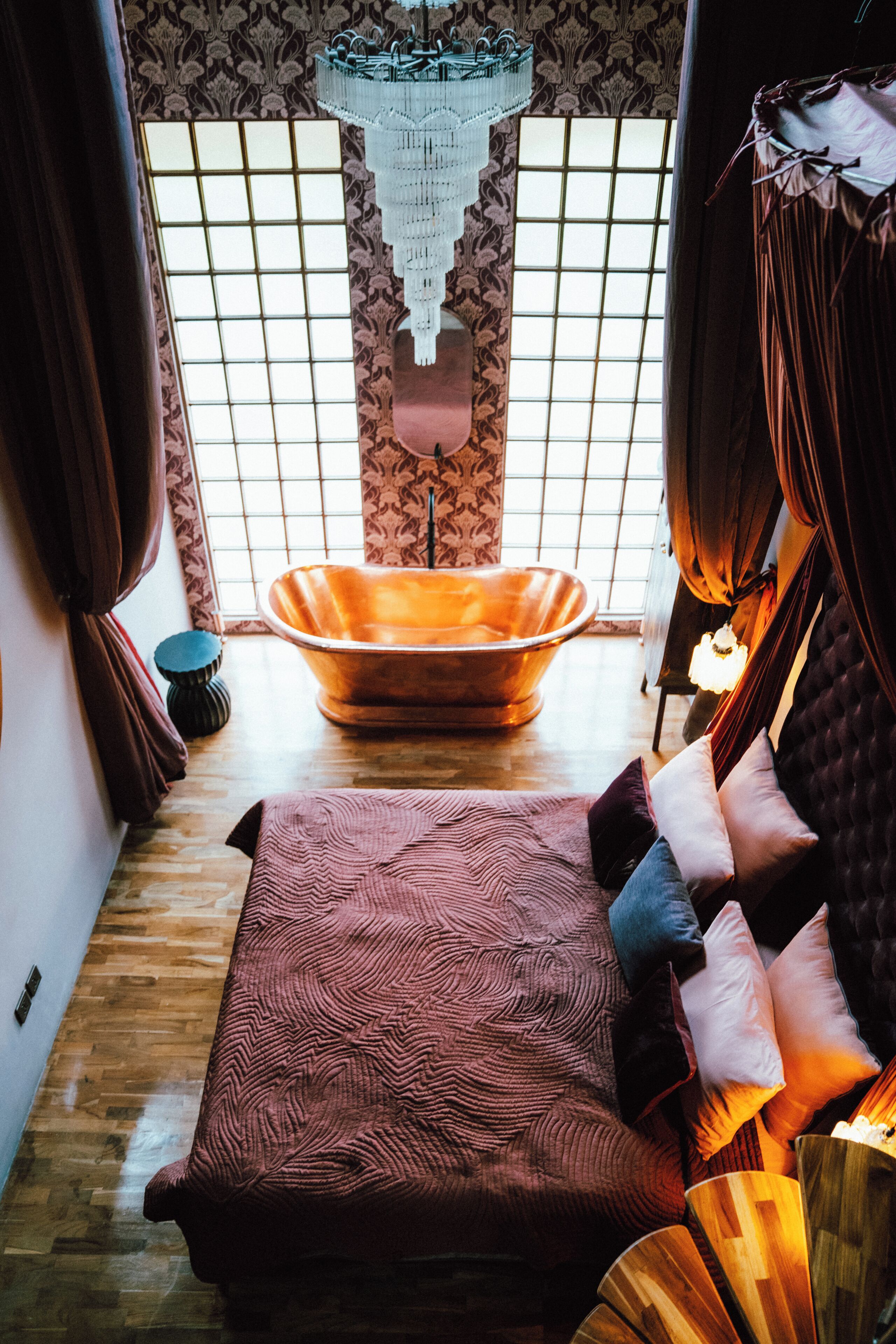 A room with a bathtub, a bed with multiple pillows, a patterned wall, and a hanging light fixture.