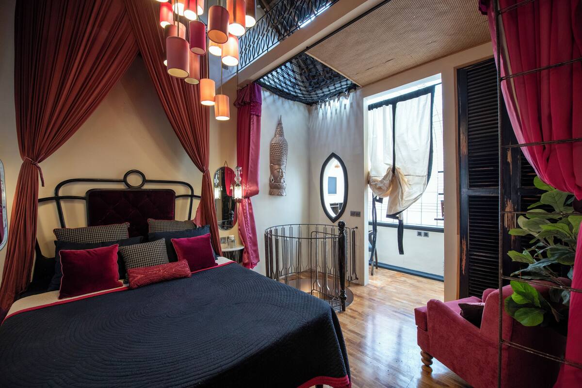 A bedroom with a bed, curtains, a window, a mirror, and a plant.