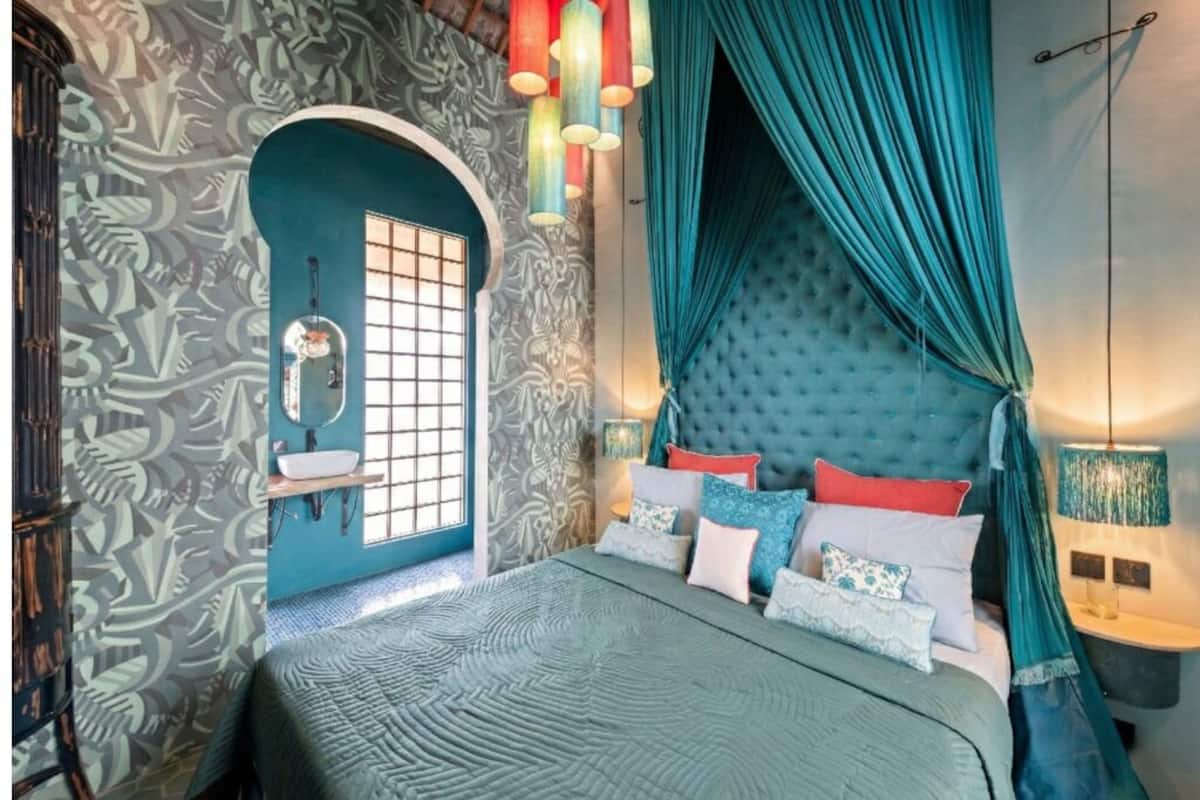 A bedroom with a large bed, a window with curtains, a mirror, and a wall with a leaf pattern.