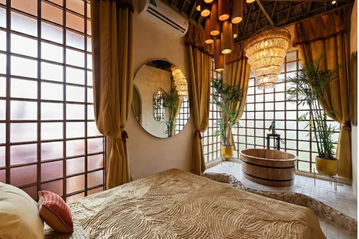 A room with a large bed, a round mirror, a wooden bathtub, and potted plants.
