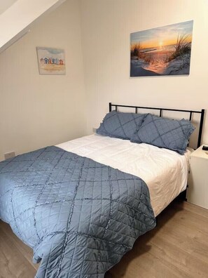 Ein Schlafzimmer mit einem Bett, einem Gemälde und einem kleinen weißen Schrank.