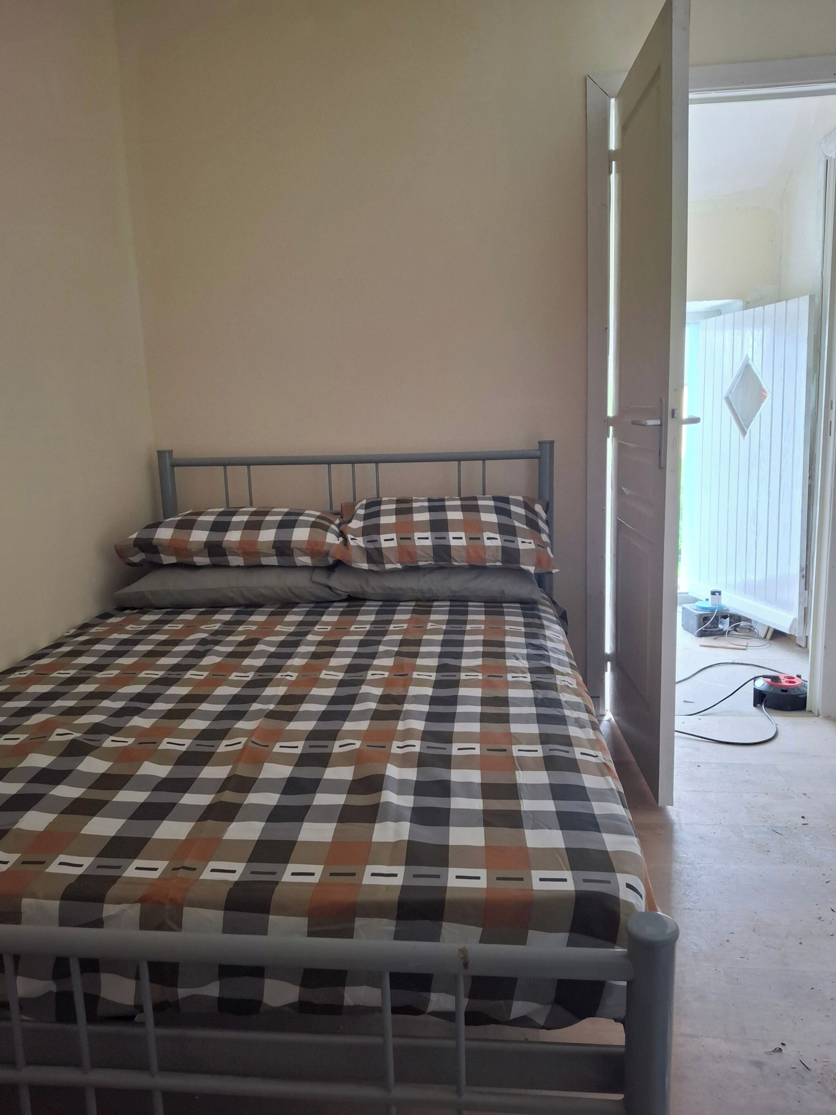 A single bed with a metal frame, a checkered bedspread, and two pillows.
