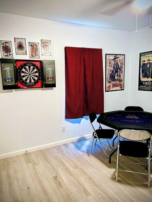 Ein Zimmer mit Dartscheibe, gerahmten Spielkarten, einem Poster und einem Pokertisch.