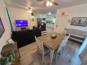 Un salón moderno con un sofá, una mesa de comedor con sillas, un televisor y una cocina al fondo.