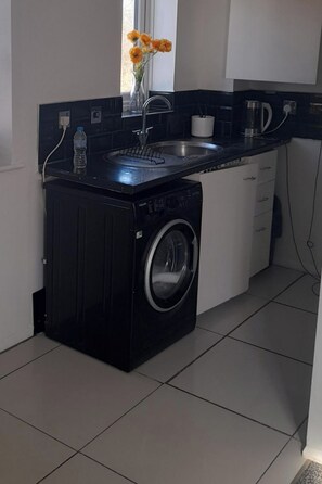 A compact kitchen with a washing machine, a sink, and a window with flowers.