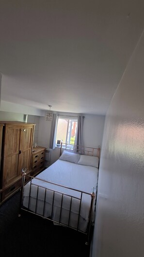 A bedroom with a bed, a wooden wardrobe, and a window with curtains.