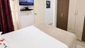 Een hotelkamer met een bed, een aan de muur bevestigde televisie, een kledingkast en een deur met een gordijn.