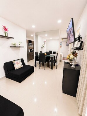 A modern living room with a black sofa, a dining area with a table and chairs, a TV mounted on the wall, and a kitchen in the background. - Condominium in Cartagena (Cartagena de Indias)