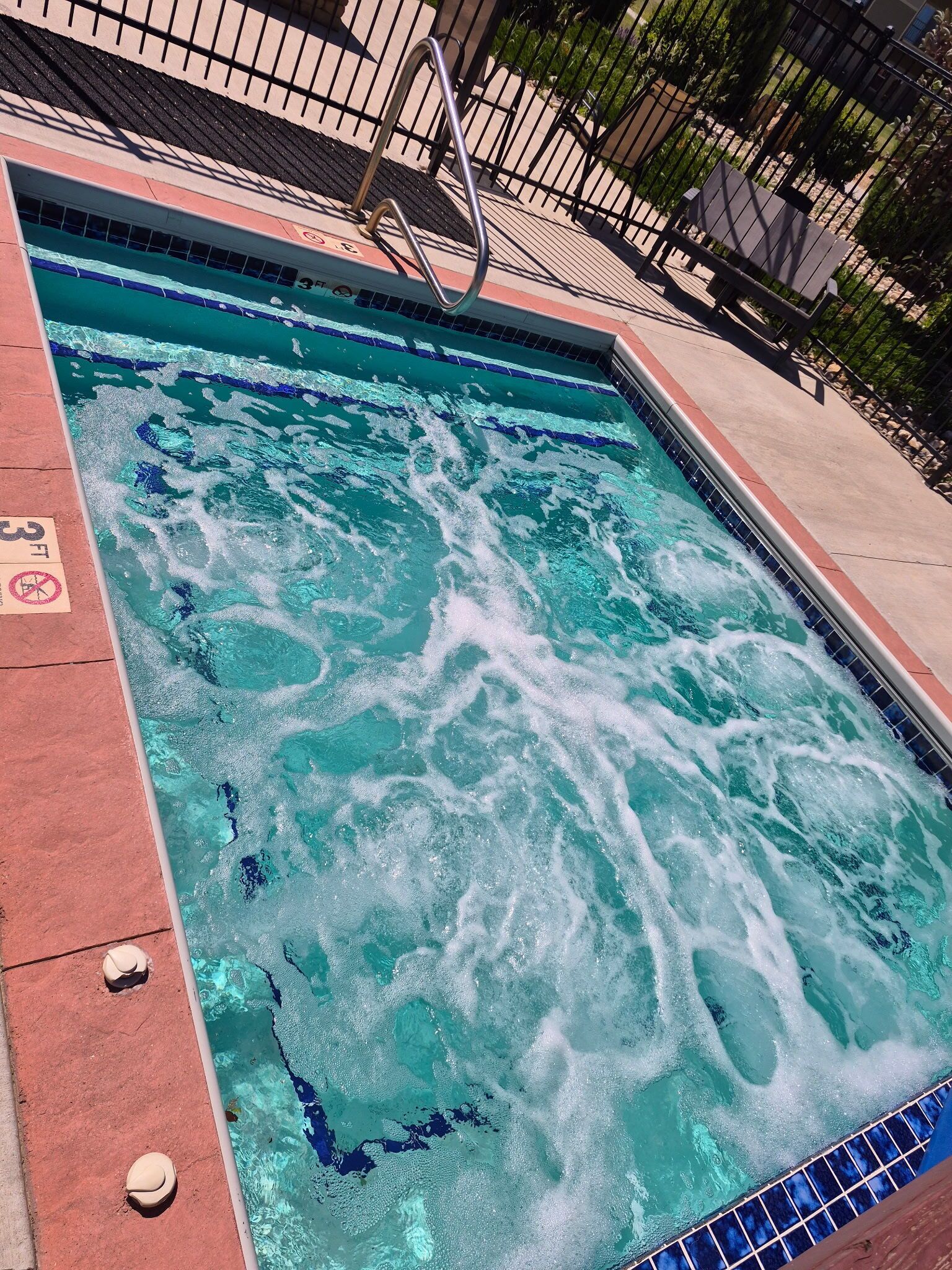 Une piscine rectangulaire avec un bord carrelé, une échelle en métal et un panneau indiquant une profondeur de 3 pieds.