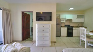 A hotel room with a bed, a white dresser, a television, a kitchen area with a microwave, stove, and cabinets. - Roy Arias Suites (Santo Domingo)