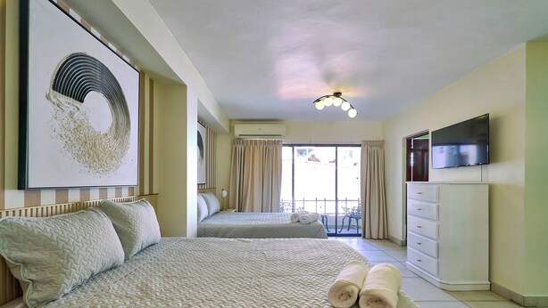 A hotel room with two beds, a TV, a dresser, and a balcony with curtains. - Roy Arias Suites (Santo Domingo)