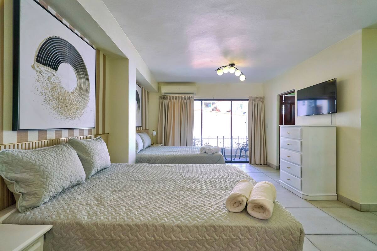 A hotel room with two beds, a TV, a dresser, and a balcony with curtains.