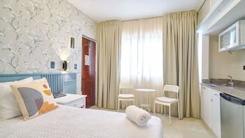 A hotel room with a bed, a desk, two chairs, a small table, and a kitchenette.