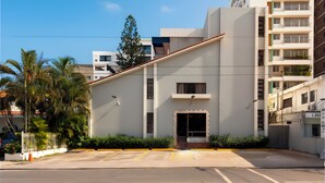 A modern building with a flat roof, a small entrance, and a parking lot in front. - Roy Arias Suites (Santo Domingo)