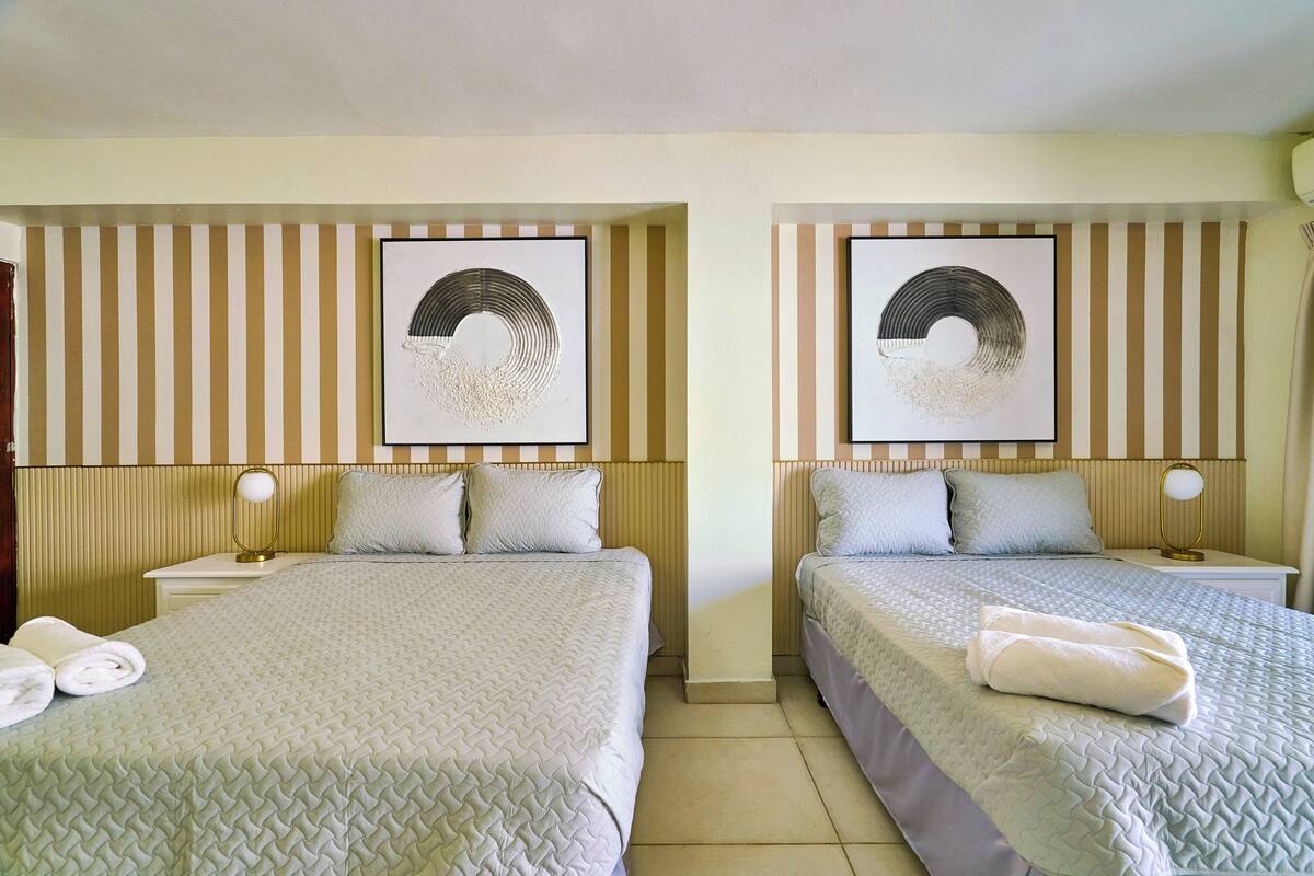 A hotel room with two beds, striped headboard panels, and wall art.