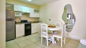 A kitchen with white cabinets, a microwave, a stove, and a dining table with chairs. - Roy Arias Suites (Santo Domingo)